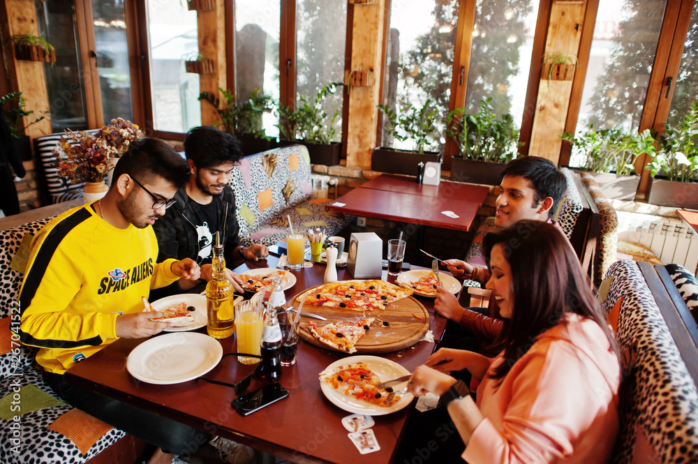 Group of asian friends eating pizza during party at pizzeria. Happy indian people having fun together, eating italian food and sitting on couch.