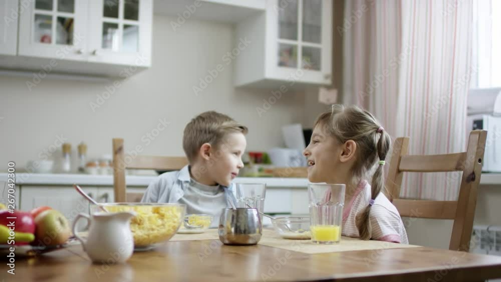 brother and sister sittin at dinner and talking when boy try to finish his snack brother and sister sittin at dinner and talking when boy try to finish his snack