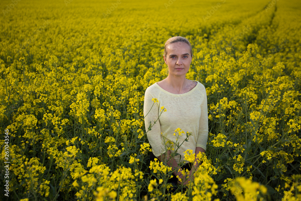 Fototapeta premium Happy woman on blooming rapeseed field in springin yellow blouse.