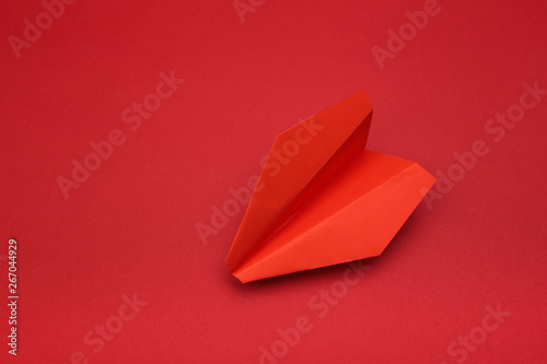 Flat lay of red paper plane on red background with text space.