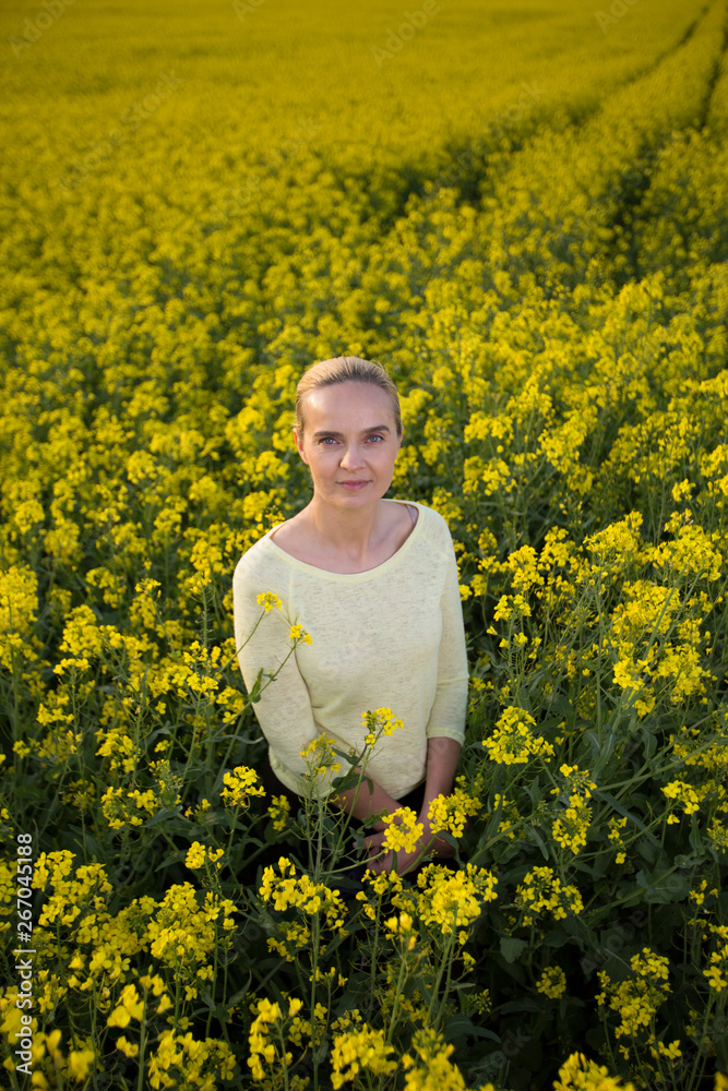 Fototapeta premium Happy woman on blooming rapeseed field in springin yellow blouse.