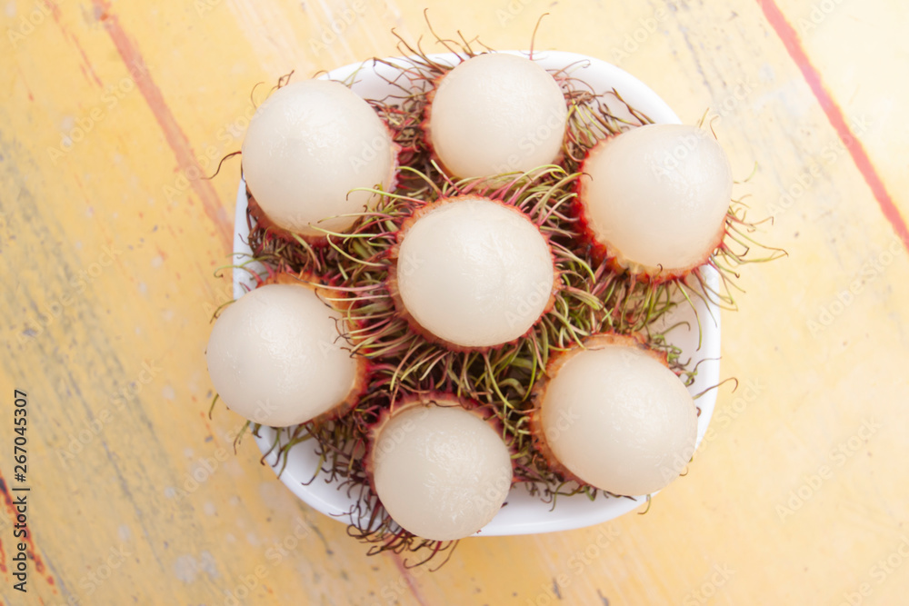 Rambutan fruits in white bowl has a delicious sweet taste on old yellow cement table background. Rambutan fruits in white bowl has a delicious sweet taste on old yellow cement table background.