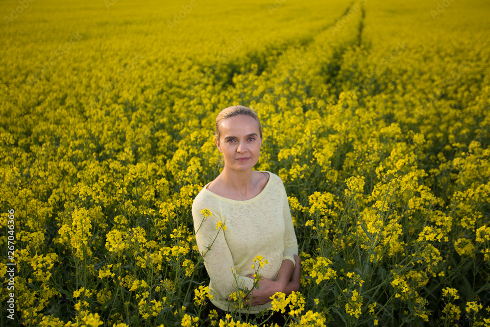 Fototapeta premium Happy woman on blooming rapeseed field in springin yellow blouse.