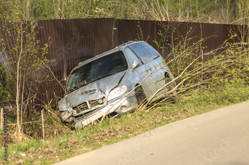 Car accident on a country road. The car is broken in front, slid into a ditch and damaged a metal fence.