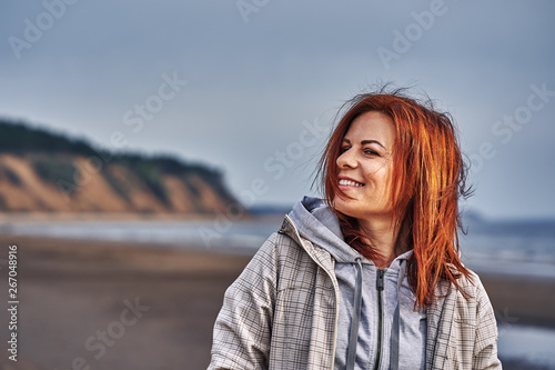Portrait of a laughing middle-aged woman with red hair walking along the river bank. Sunny spring morning. Close-up. © afefelov68