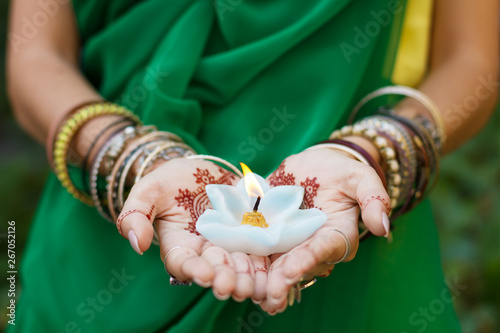 Beautiful woman in traditional Muslim Indian wedding green sari dress hands with henna tattoo mehndi pattern jewelry and bracelets hold burning lotus candle Summer culture festival celebration concept photo
