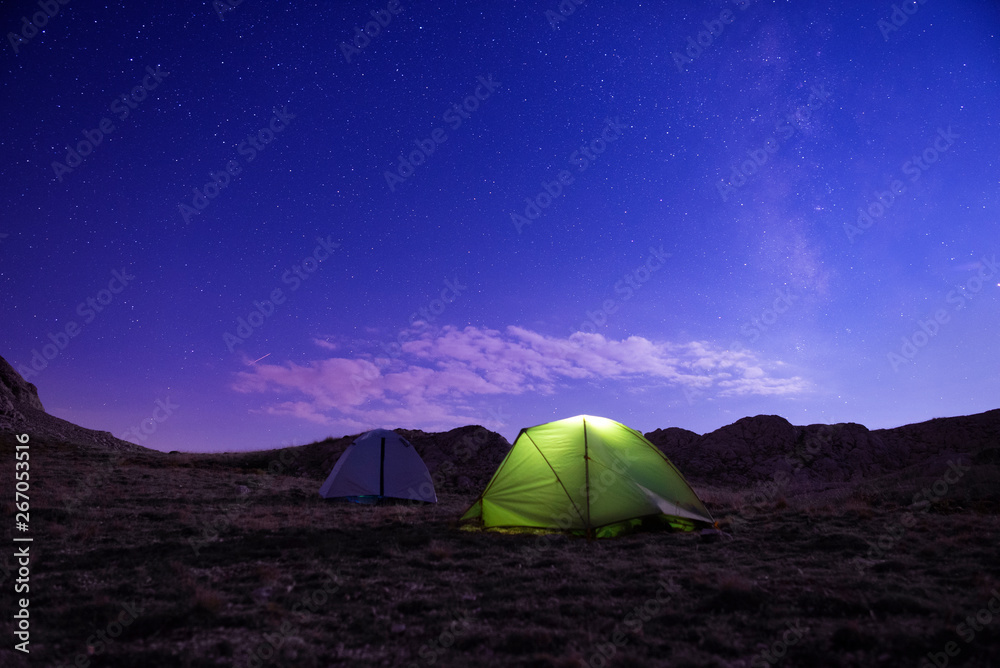 Camping tents under the amazing blue starry sky with a lot of shining stars and clouds.