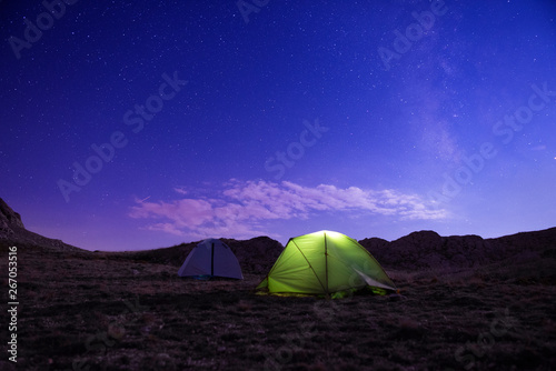 Camping tents under the amazing blue starry sky with a lot of shining stars and clouds.