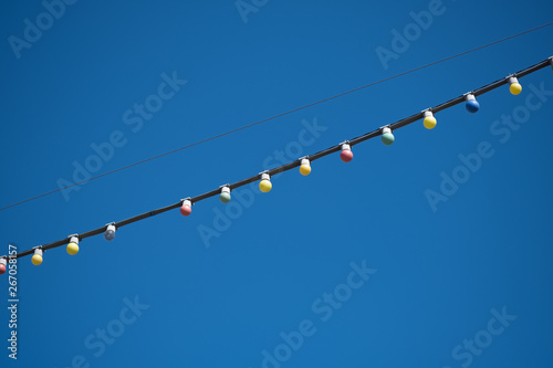 Festive decorations. Lamps on the wire to decorate the street. Picture taken against the blue sky.