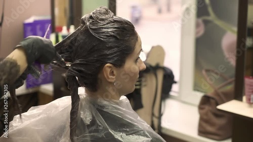 curly haired hairdresser in black shirt finishes dying long dark hair and fixes strands in front of mirror close view