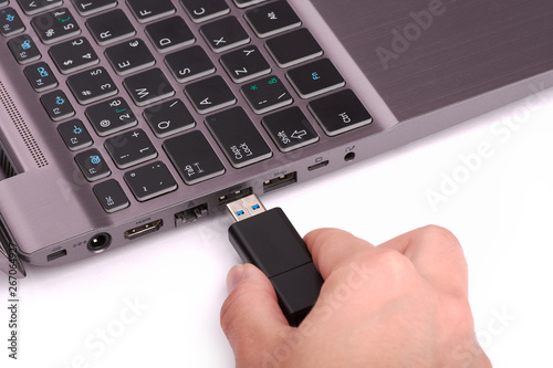 The hand of a young woman connects a USB flash drive to a port in a laptop with a black keyboard. Isolated on white background.