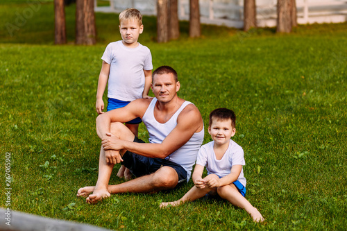brutal man and children in white t-shirts sitting on the green grass in the summer