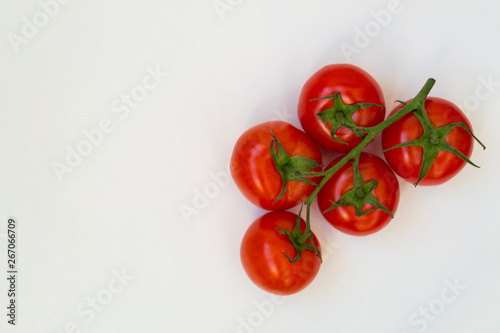 Organic red tomatoes with a green twig handful, lie on a white background. There is a place for text. © Venera
