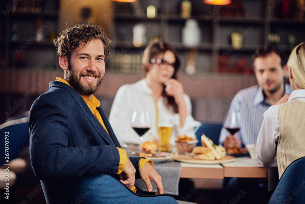 Young smiling man dressed smart casual sitting at restaurant and