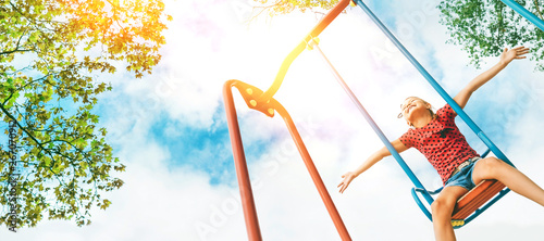  Funny smiling little girl swinging on the swing wide opened an arms with blue sky background headers web site