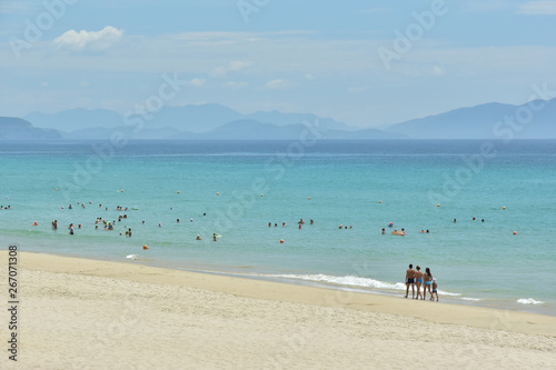 Obraz na płótnie Beautiful European clean white sand beach with blue water against the background of the cloudy sky and mountains. Family of four people walking along the coast w salonie
