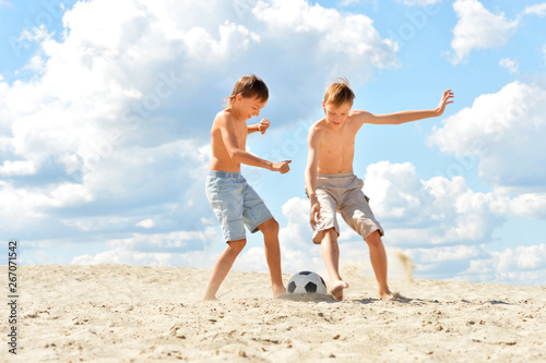 Portrait of two brothers playing football on beach in summer day