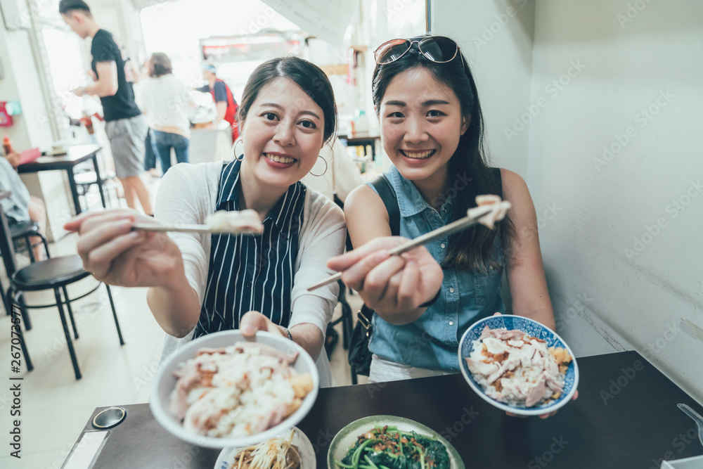 Fototapeta premium group of best sisters travel in taiwan taipei eating local meal turkey rice sharing to camera holding chopsticks sitting in vendor on summer. smiling attractive young girl friends having lunch.