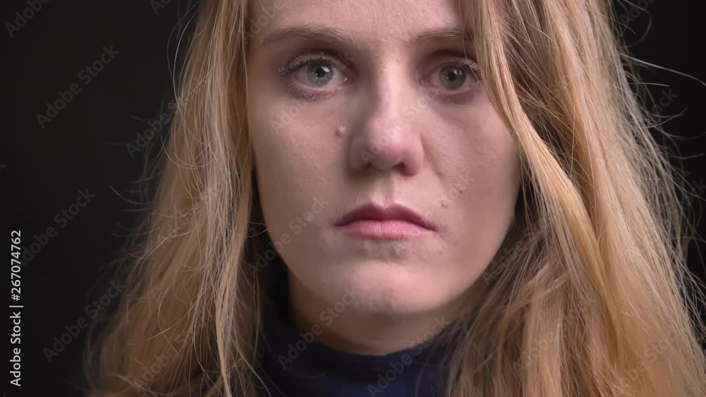 Close-up portrait of young blonde model with fuzz hair watching miserably into camera on black background.
