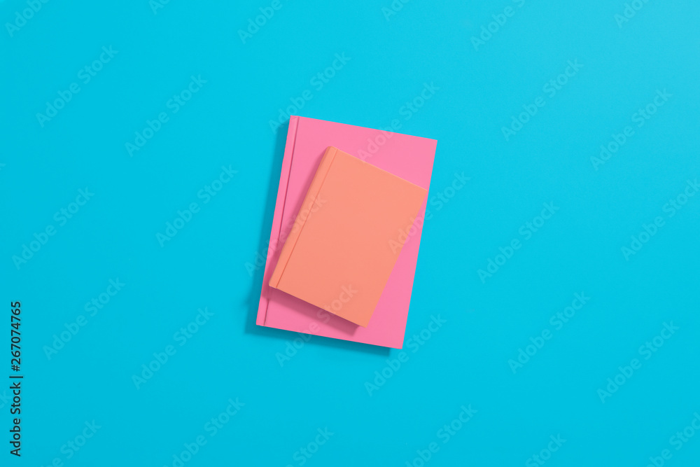 Orange and pink hardcover notebooks laying on a pastel blue background. Center composition with space for copy and text. Orange and pink hardcover notebooks laying on a pastel blue background. Center composition with space for copy and text.