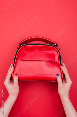Bright summer fashion ladies accessories. Stylish red leather handbag or flap bag on a red background. Women hands with bright manicure holding bag. Top View. Flat Lay. Copy Space. Mock up