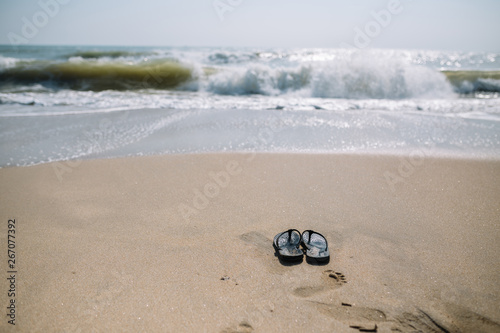 Flip flops on a sandy beach in Summer vacation with waving sea.