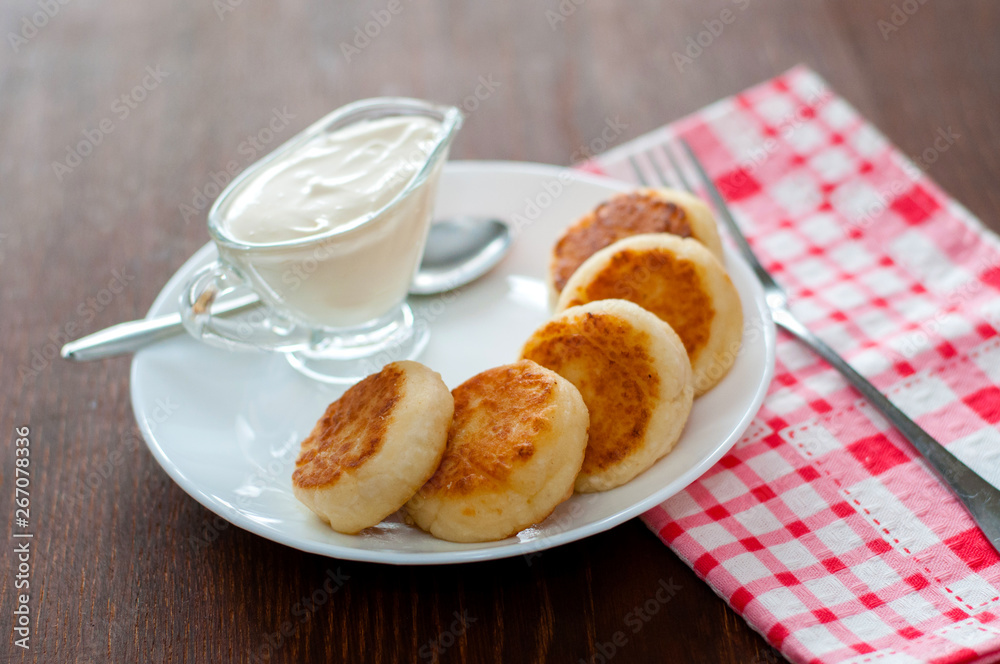 Fried cheese pancakes with sour cream on a white plate view from the top. Can be used for menu design. Fried cheese pancakes with sour cream on a white plate view from the top. Can be used for menu design.