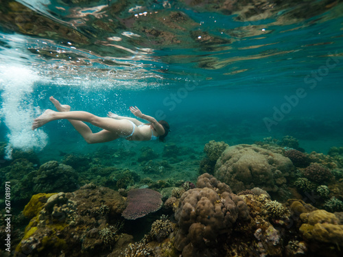 Young woman is swimming among coral reefs in shallow water.