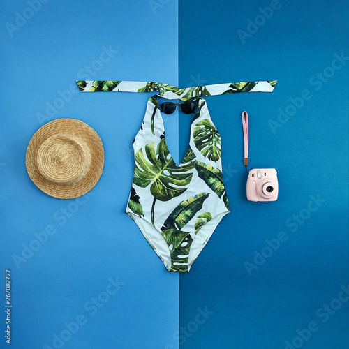 Beautiful unusual outfit presentation for fashion blog, advertising, clothing catalog. White swimsuit with a trendy print of green palm leaves. Sunglasses, summer straw hat and pink ladies' camera.