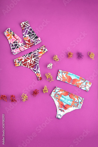 Beautiful unusual outfit presentation for fashion blog, advertising, clothing catalog. Two trendy women's swimsuit on a purple background. Multicolored dry roots for decoration. Swimsuit flatlay.