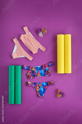 Beautiful unusual outfit presentation for fashion blog, advertising, clothing catalog. Two trendy women's swimsuit on a purple background. Rolls of colored paper and colorful dry roots for decoration.