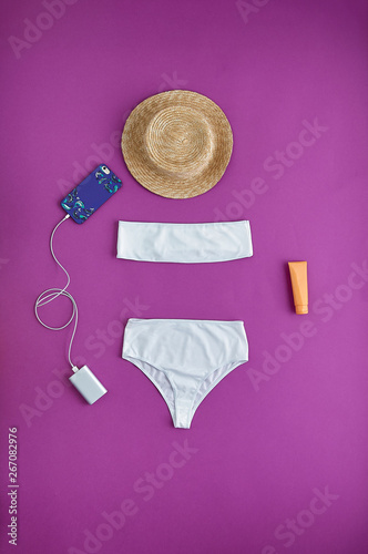 Beautiful unusual outfit presentation for fashion blog, advertising, clothing catalog. Snow-white swimsuit with top bandage. Beach accessories: phone with portable charging, hat, sunscreen. flatlay.