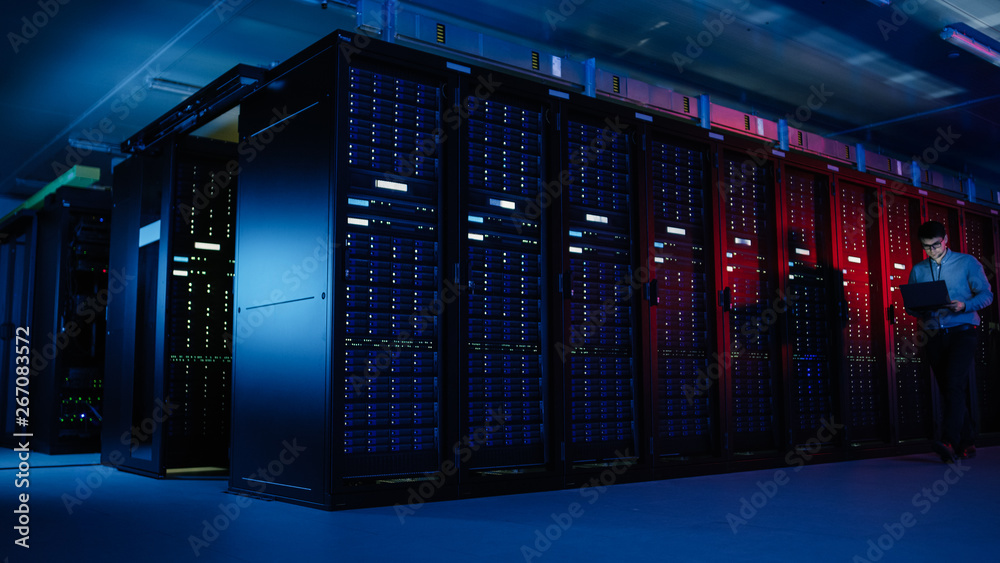 In Data Center: Male IT Specialist Walks along the Row of Operational Server Racks, Uses Laptop for Maintenance. Concept for Telecommunications, Cloud Computing, Artificial Intelligence, Supercomputer In Data Center: Male IT Specialist Walks along the Row of Operational Server Racks, Uses Laptop for Maintenance. Concept for Telecommunications, Cloud Computing, Artificial Intelligence, Supercomputer