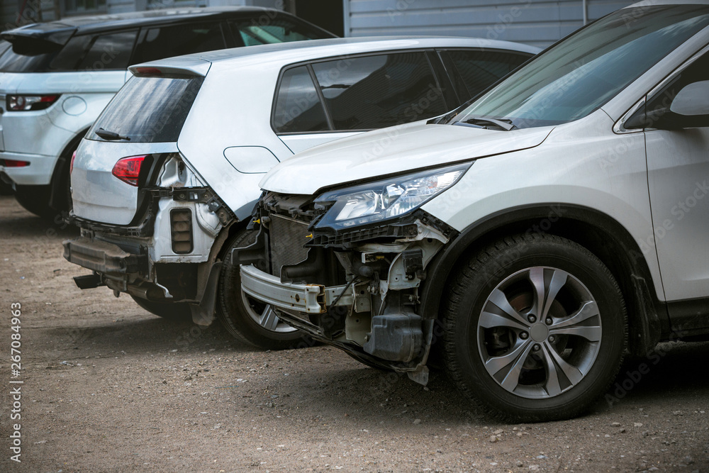 Broken and crashed modern cars after an accident on street, damaged automobile after collision at the city road. Needed tow truck for going to repairs service.