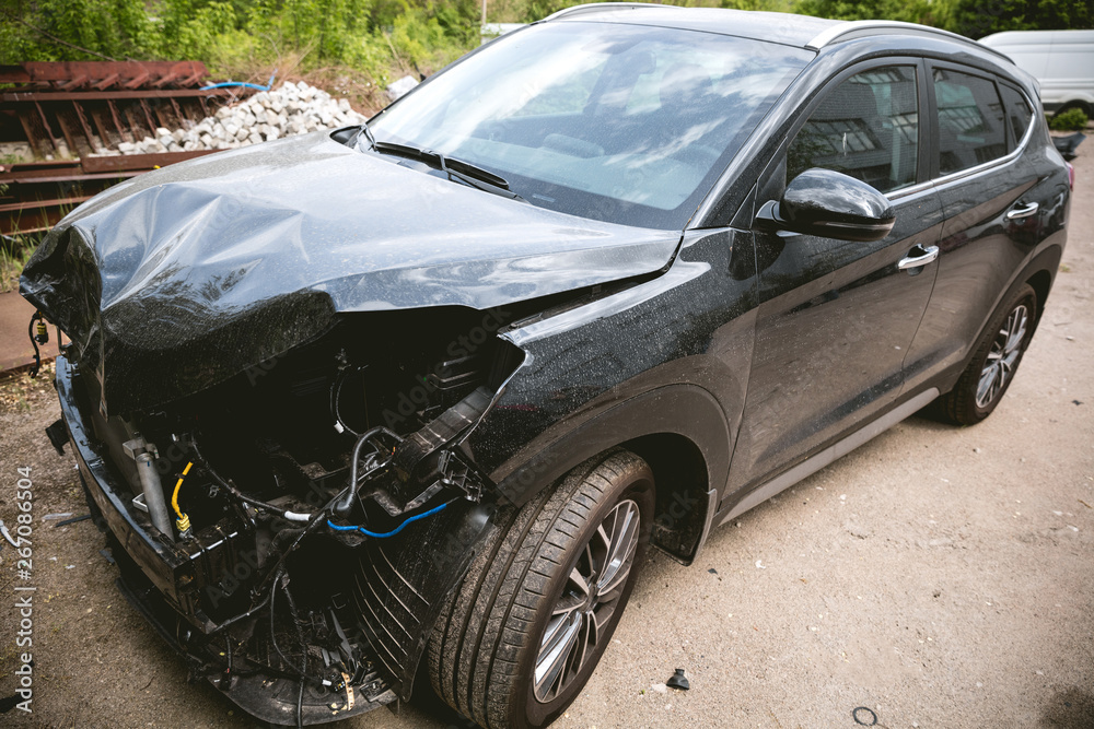 Broken and crashed modern black car after an accident on street, damaged automobile after collision at the city road. Needed tow truck for going to repairs service.