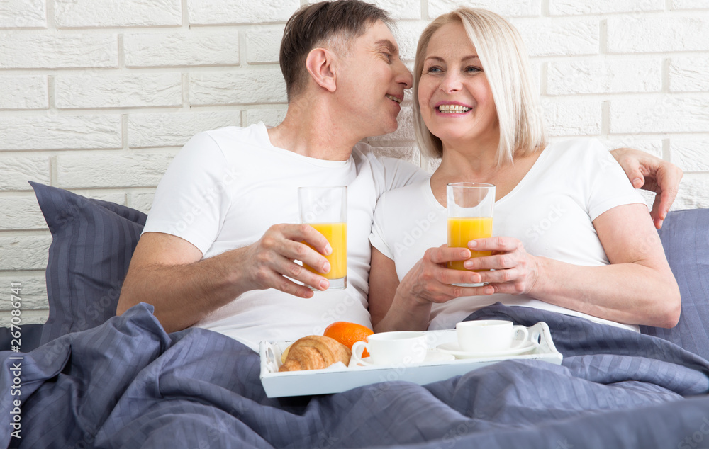 Happy middle aged couple having breakfast in the bed at hotel