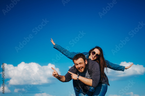 Couple in love flying arms out to the sides against the blue sky with white clouds in the summer