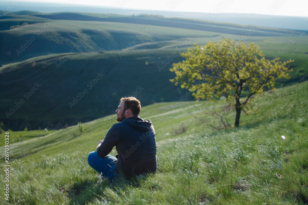 A man travels on vacation, sitting on the grass on the mountain looking into the distance to the mountains