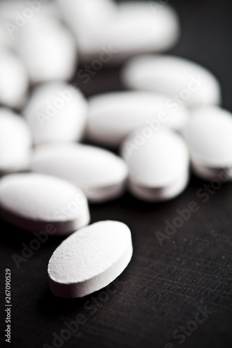 Pile of white drug pills laying on black board background.