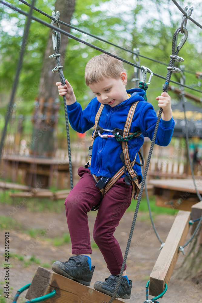 A little boy is training in a rope park. The child climbs the obstacle course. Active recreation in the park in the fresh air.