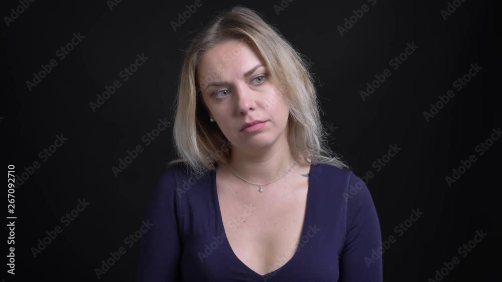 Blonde businesswoman in blue blouse with scoop neckline watching in thoughtfully perplexity into camera on black background. Blonde businesswoman in blue blouse with scoop neckline watching in thoughtfully perplexity into camera on black background.