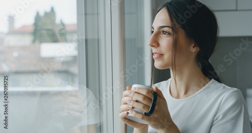 Portrait of a pensive young woman is drinking a tea and looking through the window in the morning in the kitchen. photo