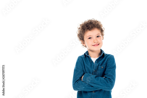 smiling curly kid in denim shirt standing with crossed arms isolated on white