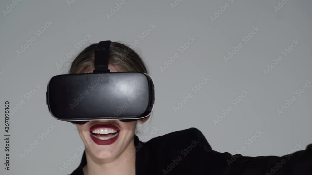 Woman playing VR device. VR glasses open the world to new games and abilities. technology, virtual reality, entertainment and people concept - happy young woman with virtual reality headset. Red lips. Woman playing VR device. VR glasses open the world to new games and abilities. technology, virtual reality, entertainment and people concept - happy young woman with virtual reality headset. Red lips.