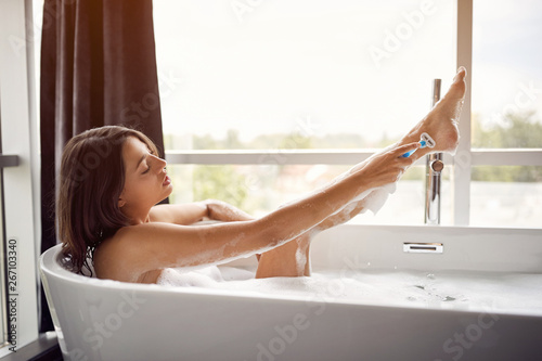 Young lady shaving her legs in the bath .