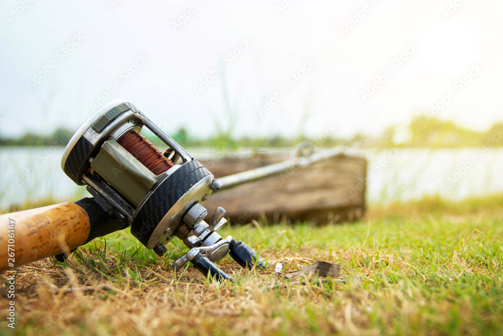 Fishing activities. rod with baitcasting reel on the grass wait for the  fish to stick or eat to the hook on natural white sky background and copy  space. Stock Photo