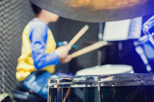 wooden drumsticks in hands of Asian kid wearing blue and yellow t-shirts to learning and play drum set in music room