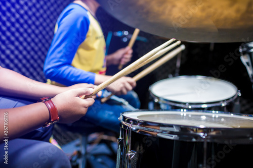 hands of teacher with wooden drumsticks guiding boy in drum learning tutorial in recording studio at music academy