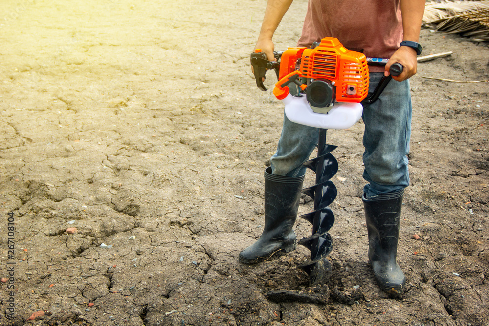 farmer using tools hand-held soil hole drilling machine or portable manual  earth auger for prepare the soil for planting trees with soil mold  background organic farming and copy space. Stock Photo