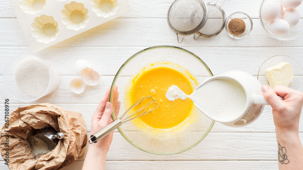 Cropped view of woman pouring milk in liquid dough on table with ingredients Cropped view of woman pouring milk in liquid dough on table with ingredients
